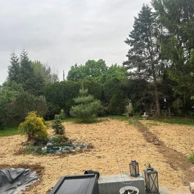 Cleared residential lot with graded earth and crushed rock base, mature trees in background