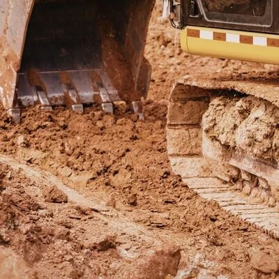 Excavator bucket digging and moving brown soil at active construction site