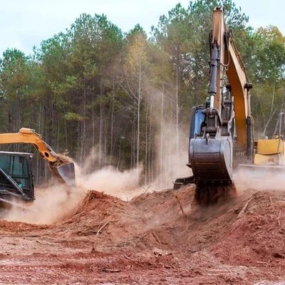 Excavators clearing wooded land with heavy equipment moving red clay soil